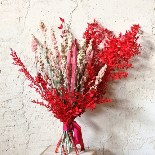 Ramo de flores secas Eros en rojo intenso, rosa y crema sobre pared clara
