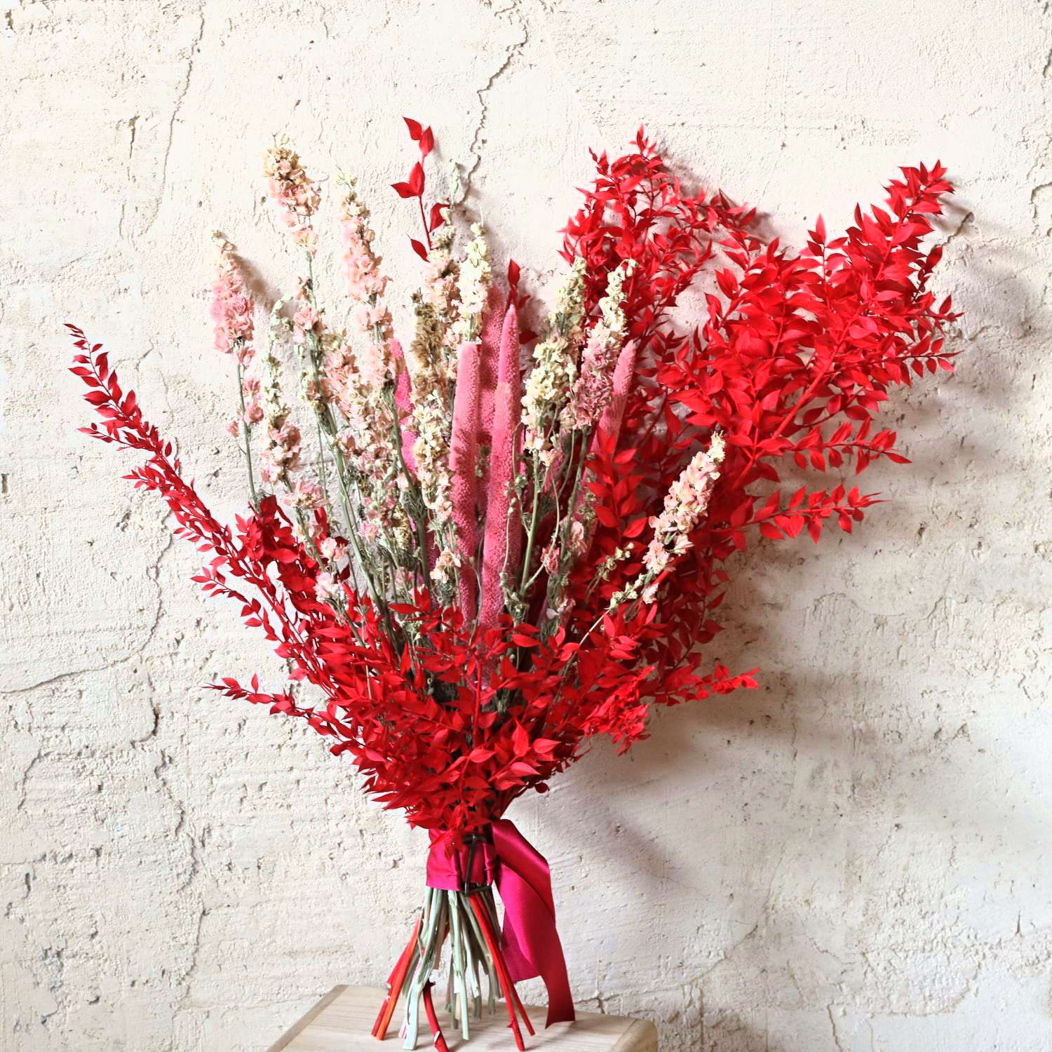 Ramo de flores secas Eros en rojo intenso, rosa y crema sobre pared clara