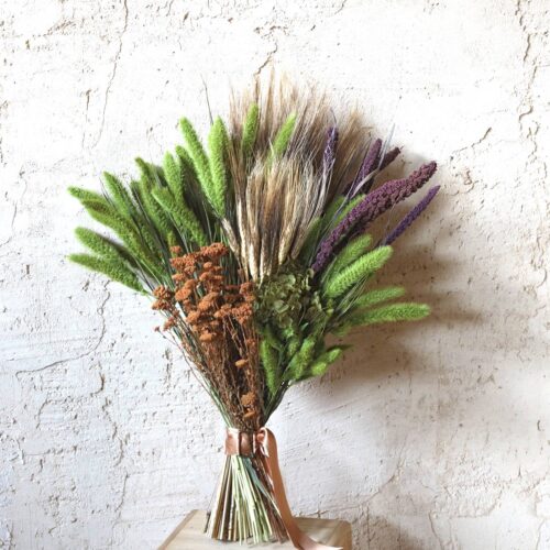 Ramo de flores secas Natur en verde lima, morado y cobre sobre pared clara