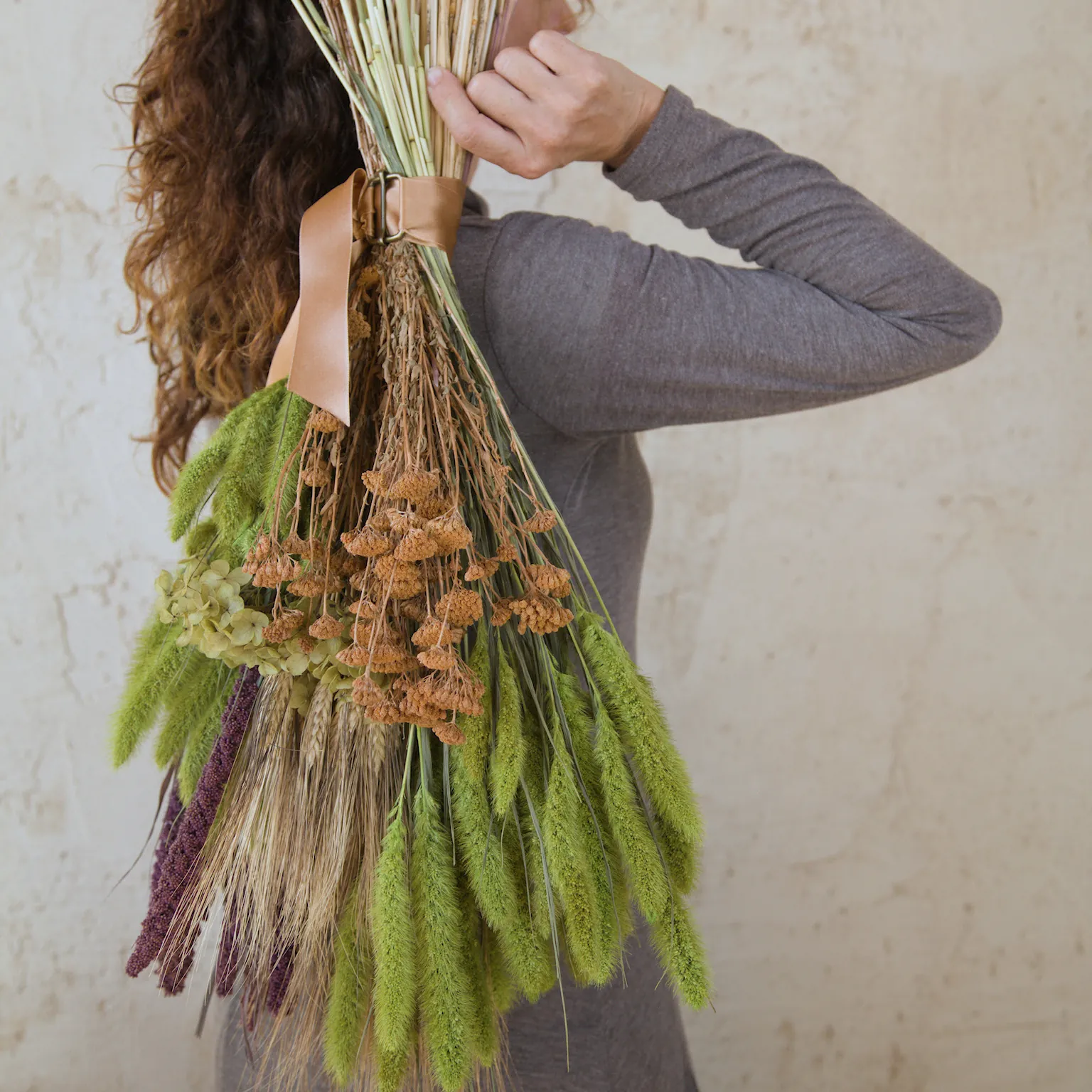 Mujer sostiene el ramo de flores secas Natur, en tonos verde lima, morado y cobre