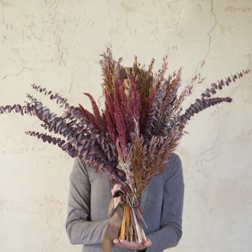 Ramo de flores secas Maroon en burdeos, castaño y ciruela sobre pared clara
